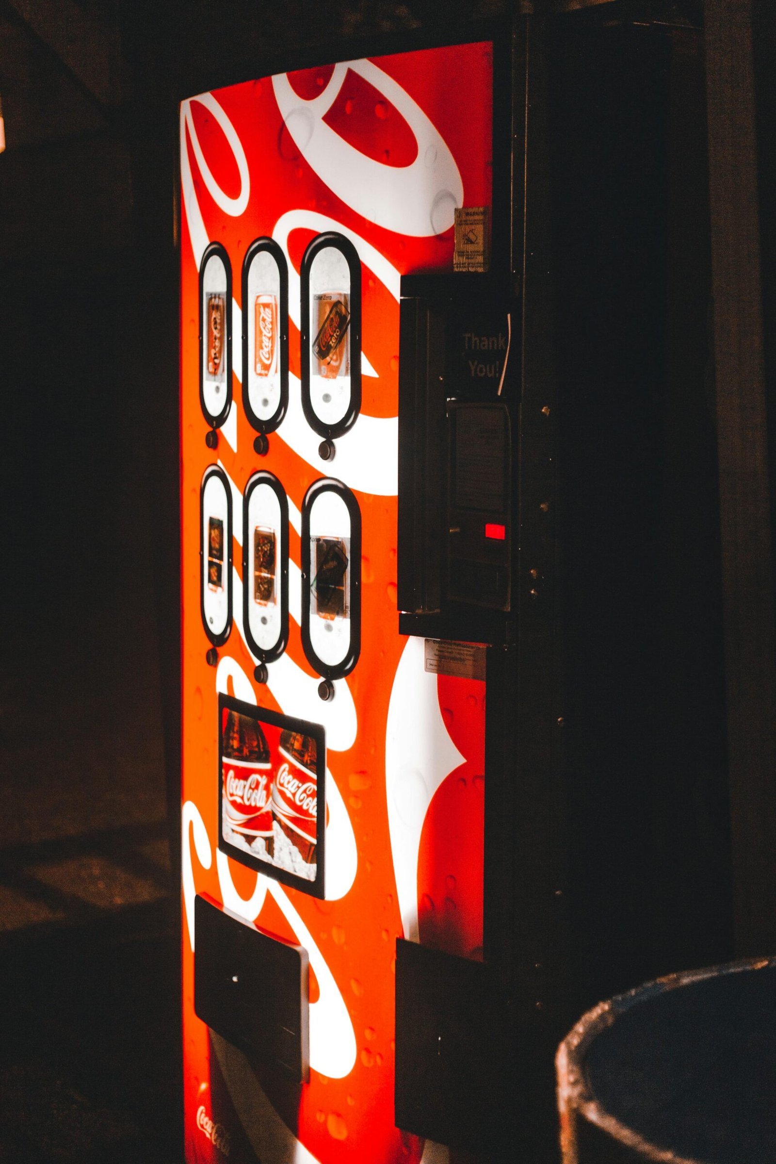 Brightly lit Coca-Cola vending machine in a dimly lit urban setting at night.